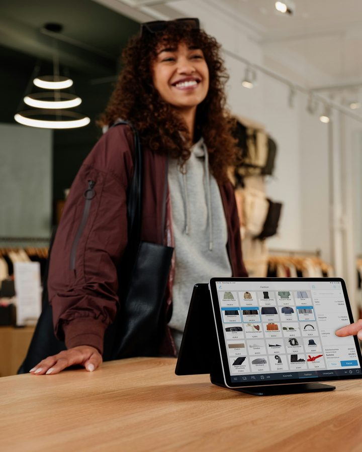 A boutique associate smiling at the counter as a customer points to an item on a tablet