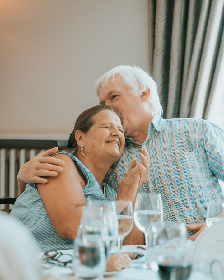 An older couple embracing at a set dinner table in a restaurant